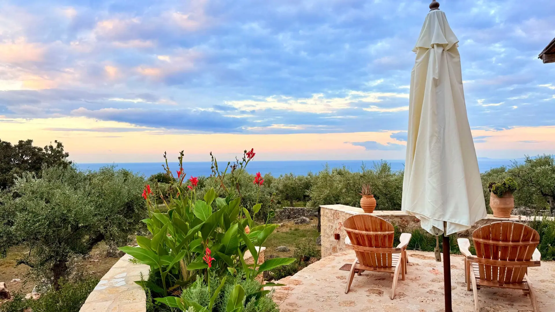 Außenansicht eines Ferienhaus in Griechenland mit Meerblick, Stühlen und Sonnenschirm. Perfekt für einen entspannten Urlaub.